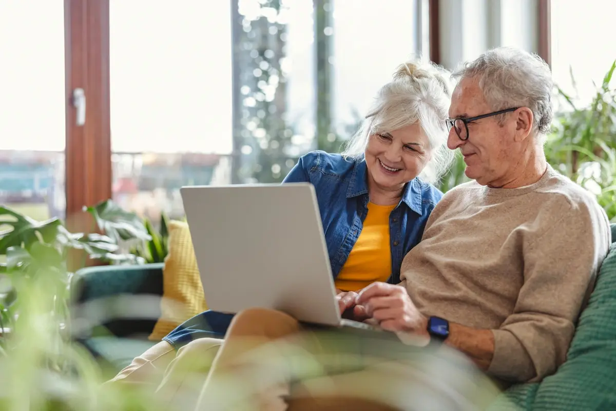 how-to-pay-for-assisted-living-senior-couple-planning Senior couple researching how to pay for assisted living on laptop at home